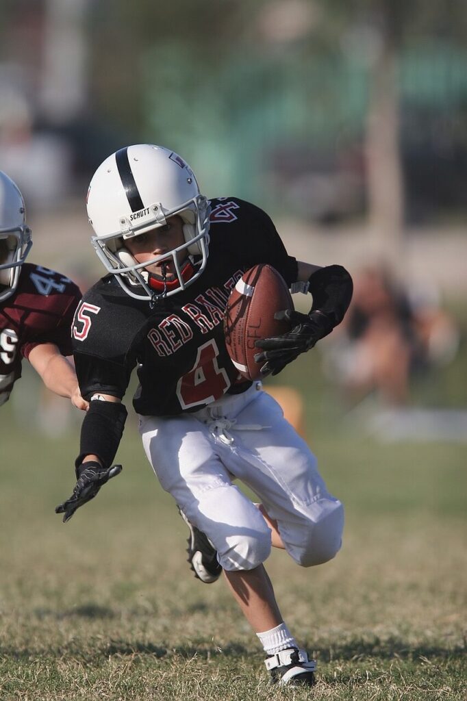 little league football player running with a ball