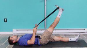 Dr. Jon deomonstrating a supine hamstring stretch lying on his back on the ground with his right leg lifted using a strap left leg straight on the ground.