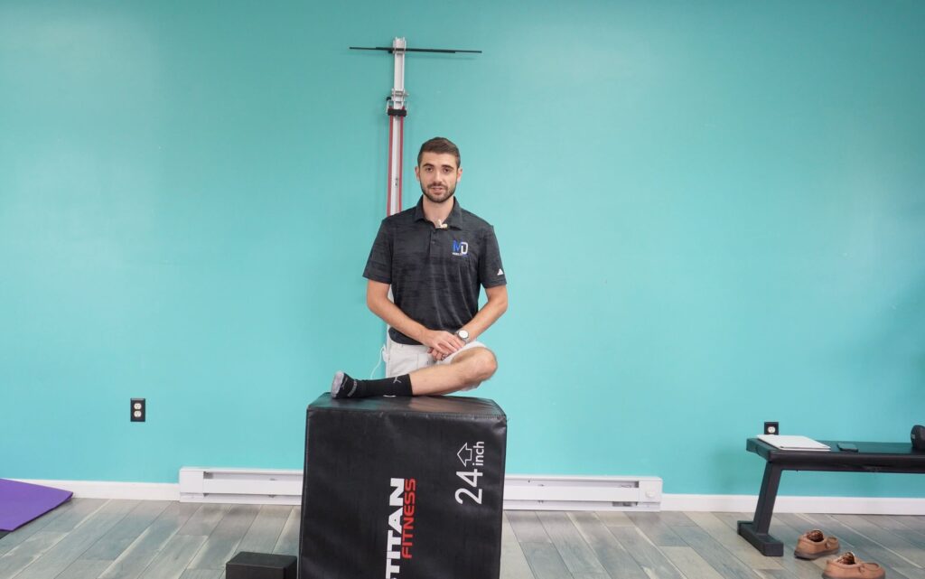 Dr. Jon demonstrating a standing pigeon stretch with his leg up on a box
