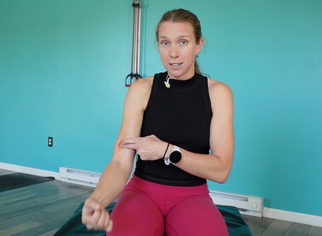 Dr. Chloe demonstrating the pin and stretch technique on her right bicep by pressing into the muscle just above the elbow with her pointer finger