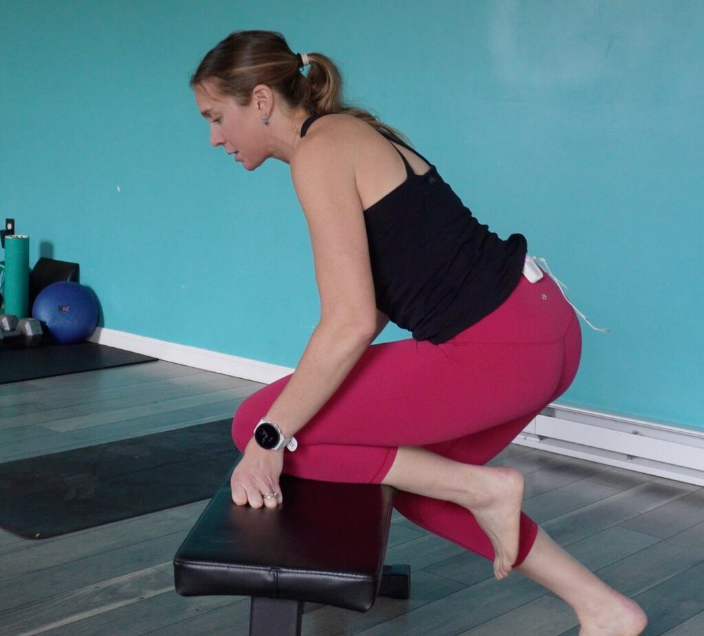 Dr. Chloe with her left knee placed on a bench, foot hanging off the back, squatting down to get a stretch through her knee as an exercise to break up knee stiffness