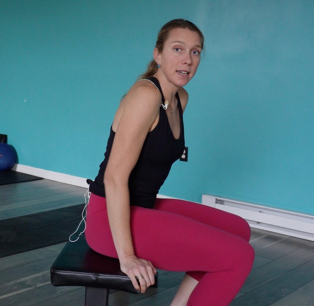 Dr. Chloe sitting on a bench with herself scooted forward heels flat on the ground to stretch the knee.