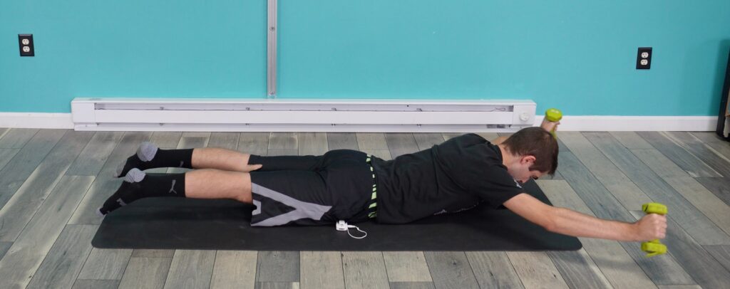 Dr. Jon doing the prone arm sweep while lying on his stomach arms stretched out overhead with light weights