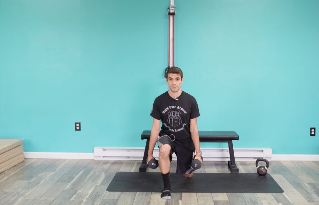 With his back left foot on a bench, dr. jon has his right foot forward hands by his sides with dumbbells in a split squat