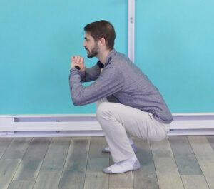 Dr. Jon in a full bodyweight squat with his feet hip width apart doing the super bowl halftime show down