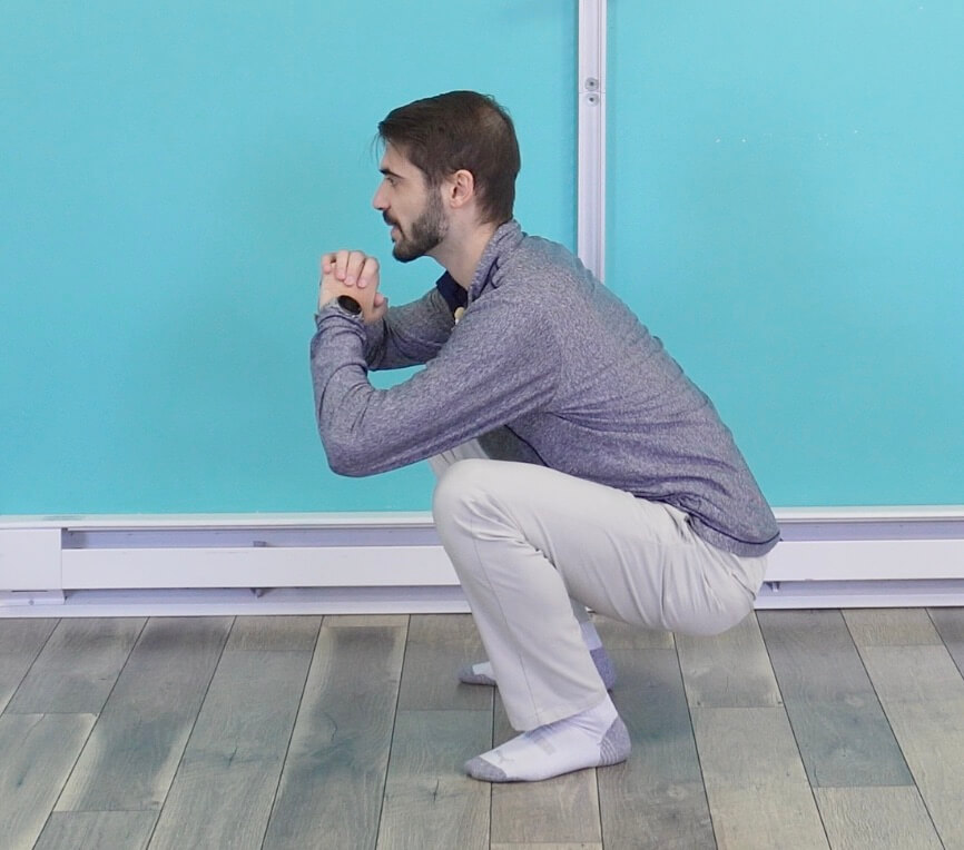 Dr. Jon in a full bodyweight squat with his feet hip width apart doing the super bowl halftime show down