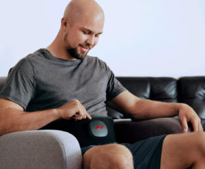 A man sitting in a chair using the hyperice venom 2 back