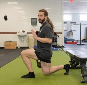 Dr. John with his left foot in front at a 90 degree angle, and his back right knee touching the ground in a split squat showing how to strengthen your hip flexors for running