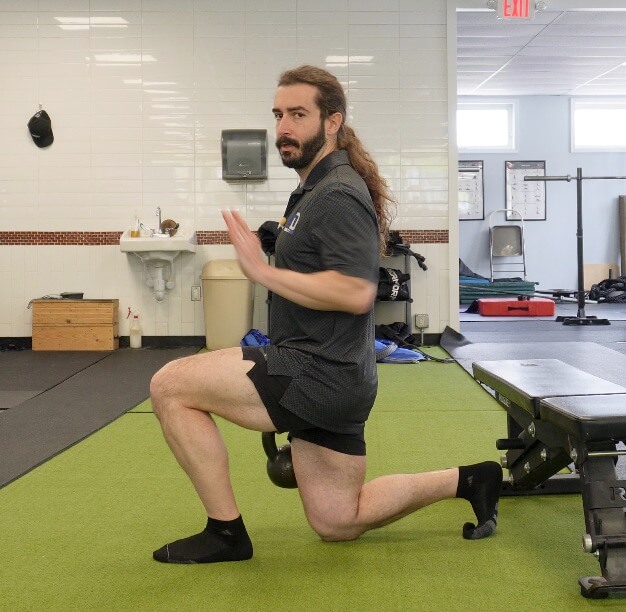 Dr. John with his left foot in front at a 90 degree angle, and his back right knee touching the ground in a split squat showing how to strengthen your hip flexors for running